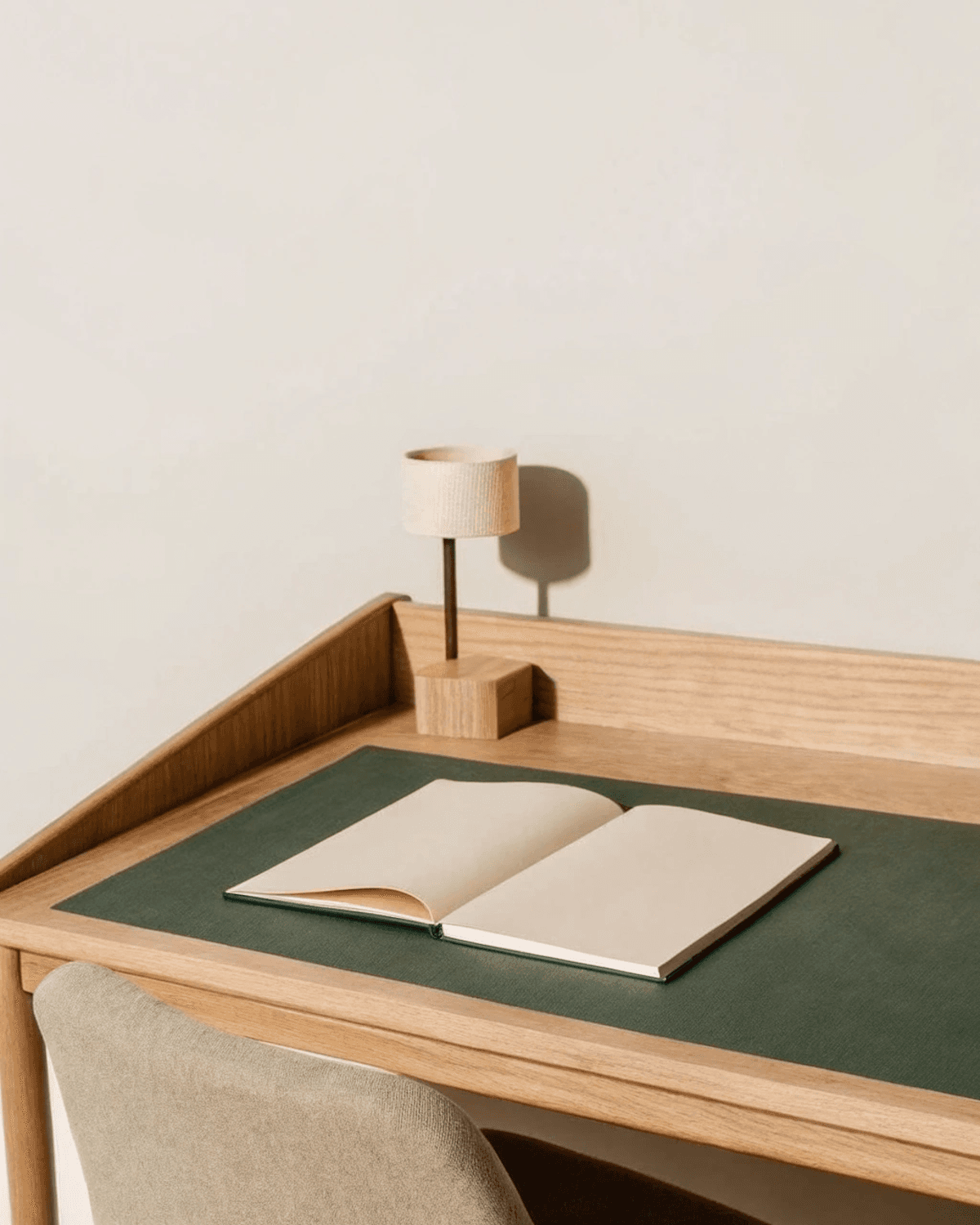 Aufgeräumter Schreibtisch aus Holz mit aufgeschlagenem Notizbuch und moderner Arbeitsleuchte